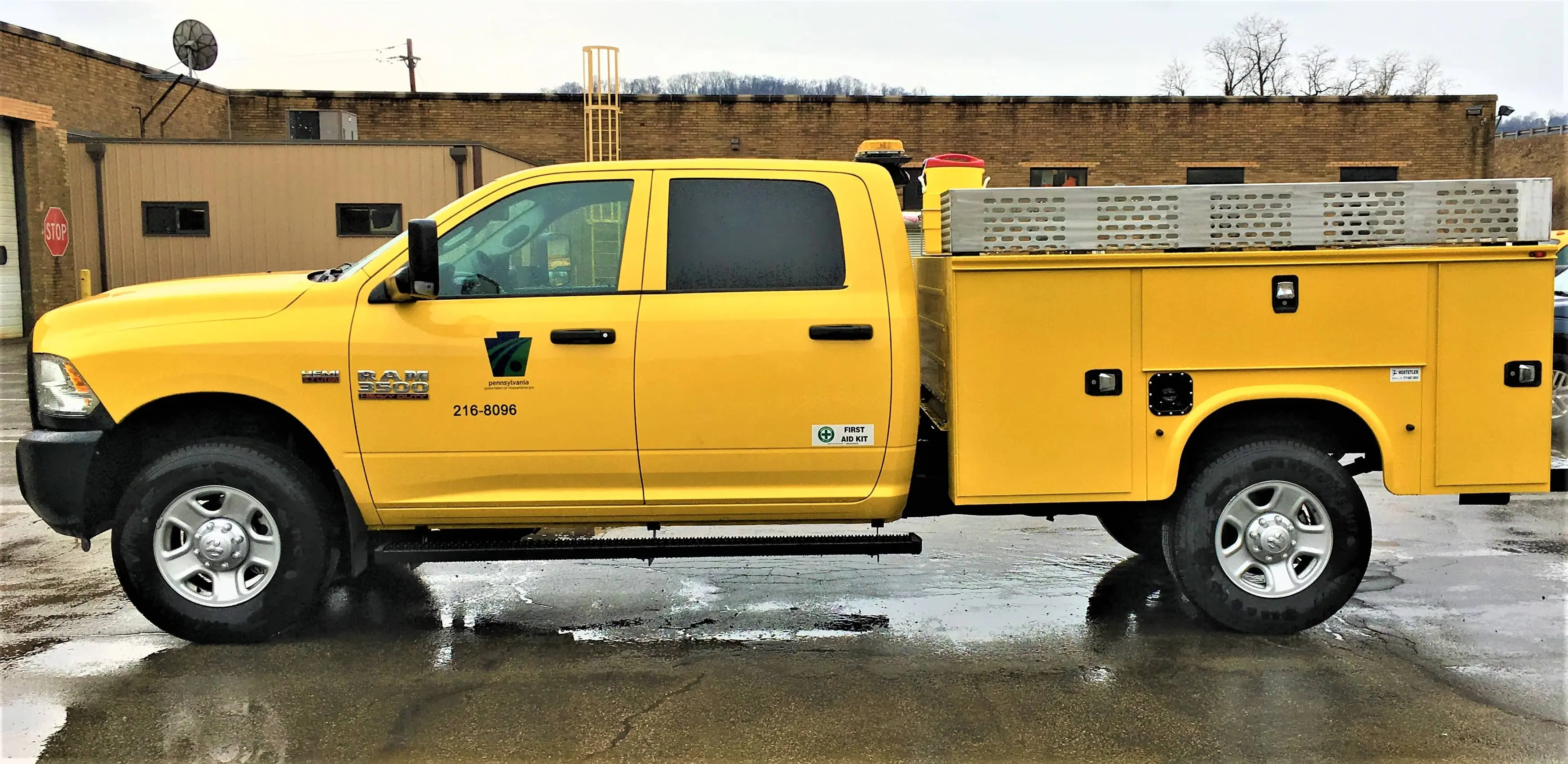 A yellow Dodge Ram 3500 crew cab truck is shown with a modified utility bed including locking compartments for tool and equipment storage.